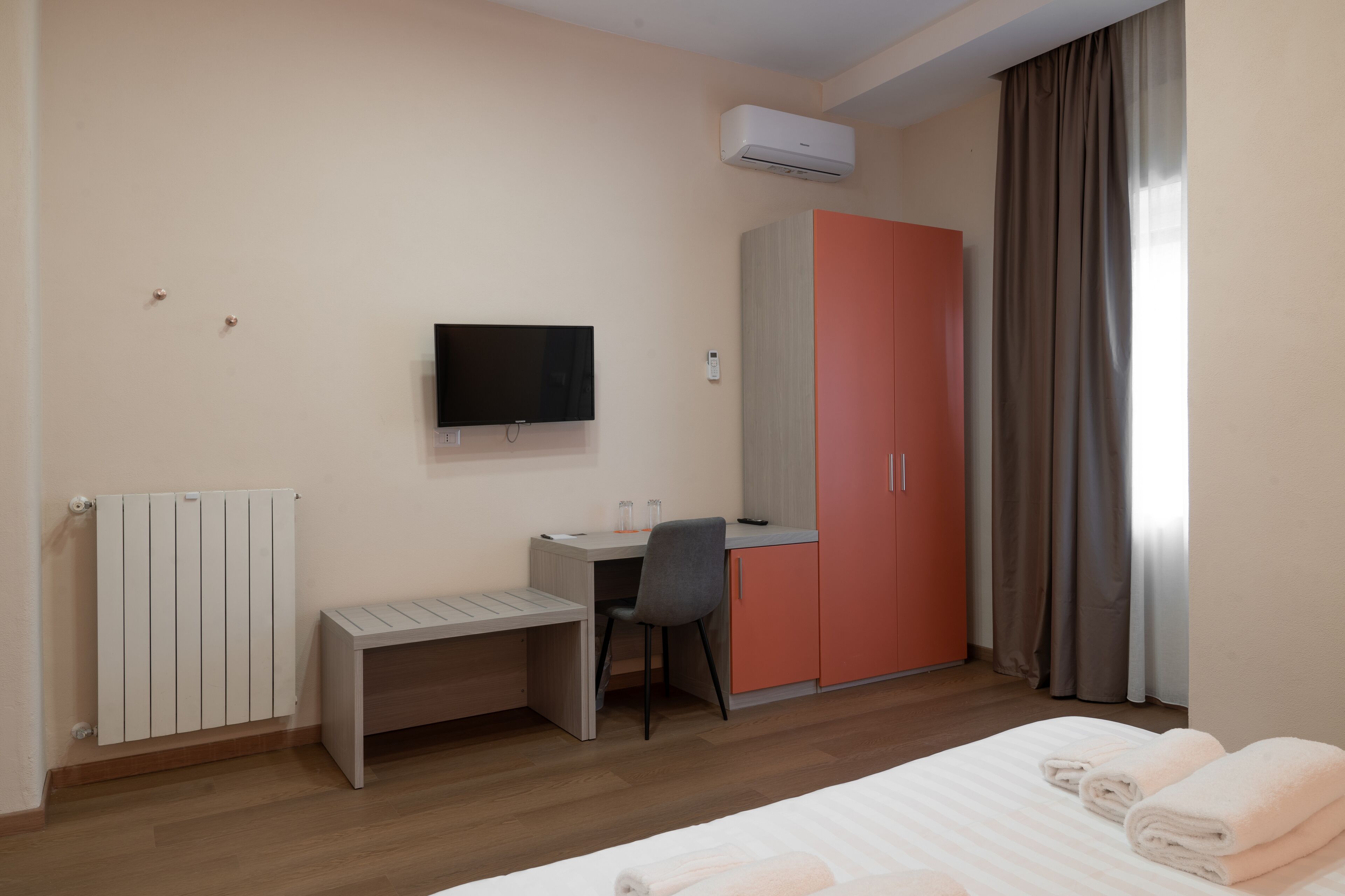 A hotel room with a bed, a desk, a chair, a television, a wardrobe, and a radiator.