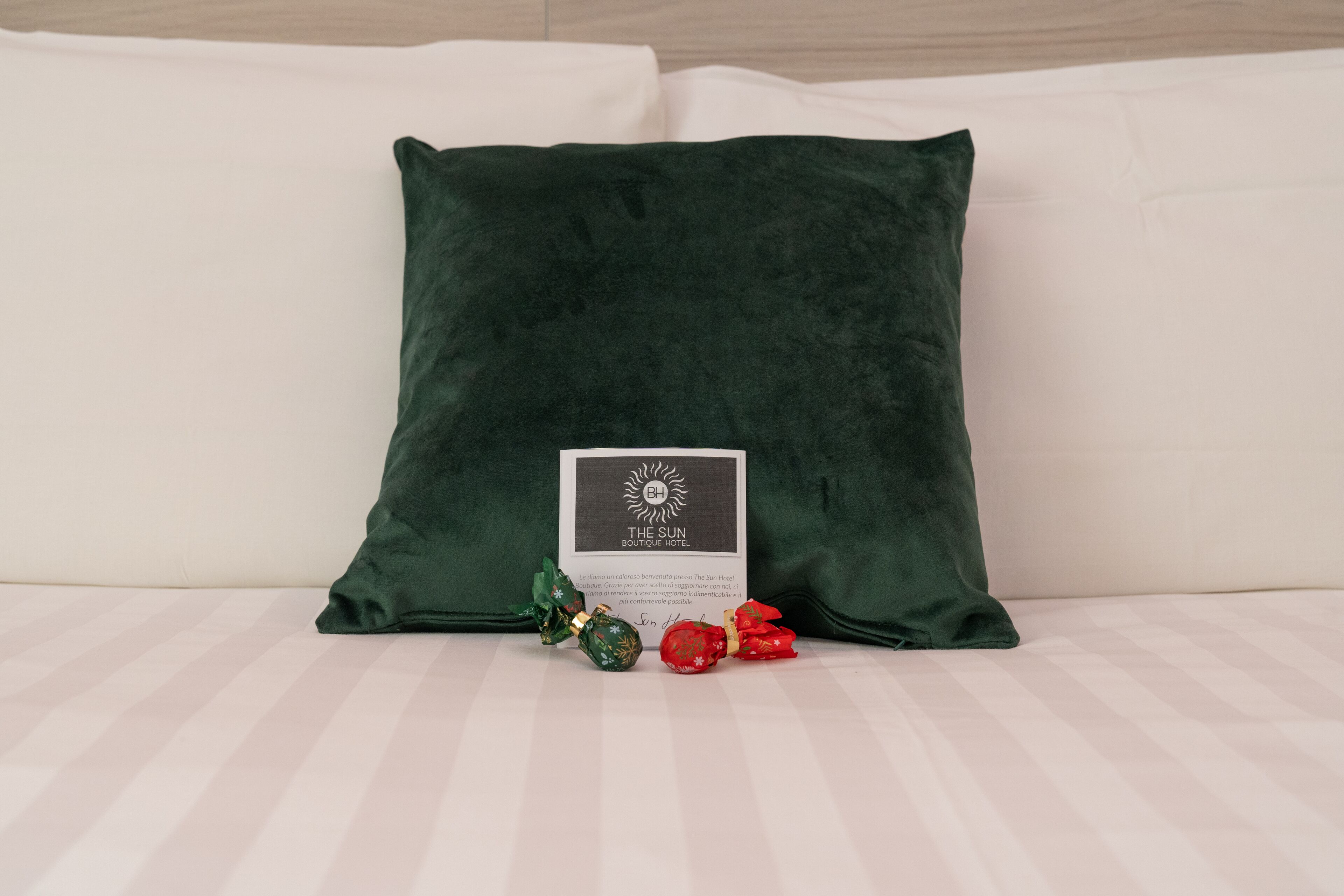 A dark green pillow on a bed with a white pillow, a card, and two wrapped gifts.