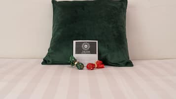 A dark green pillow on a bed with a white pillow, a card, and two wrapped gifts.
