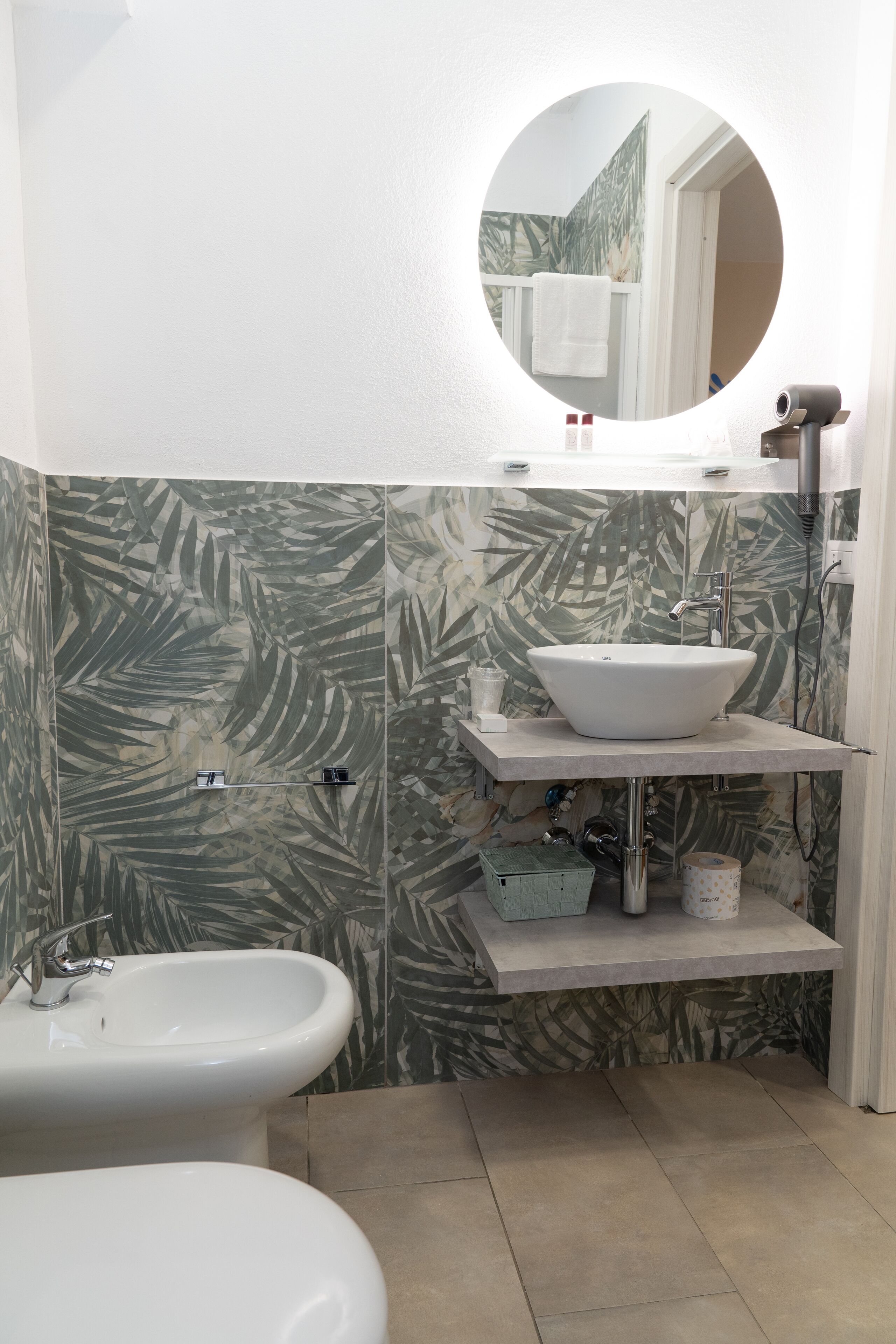 A bathroom with a large sink, a smaller sink, a mirror, and a shelf with toiletries.