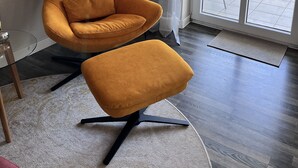 Ein modernes Wohnzimmer mit großem Fenster, einer Stehlampe, einer Couch und passendem Hocker.