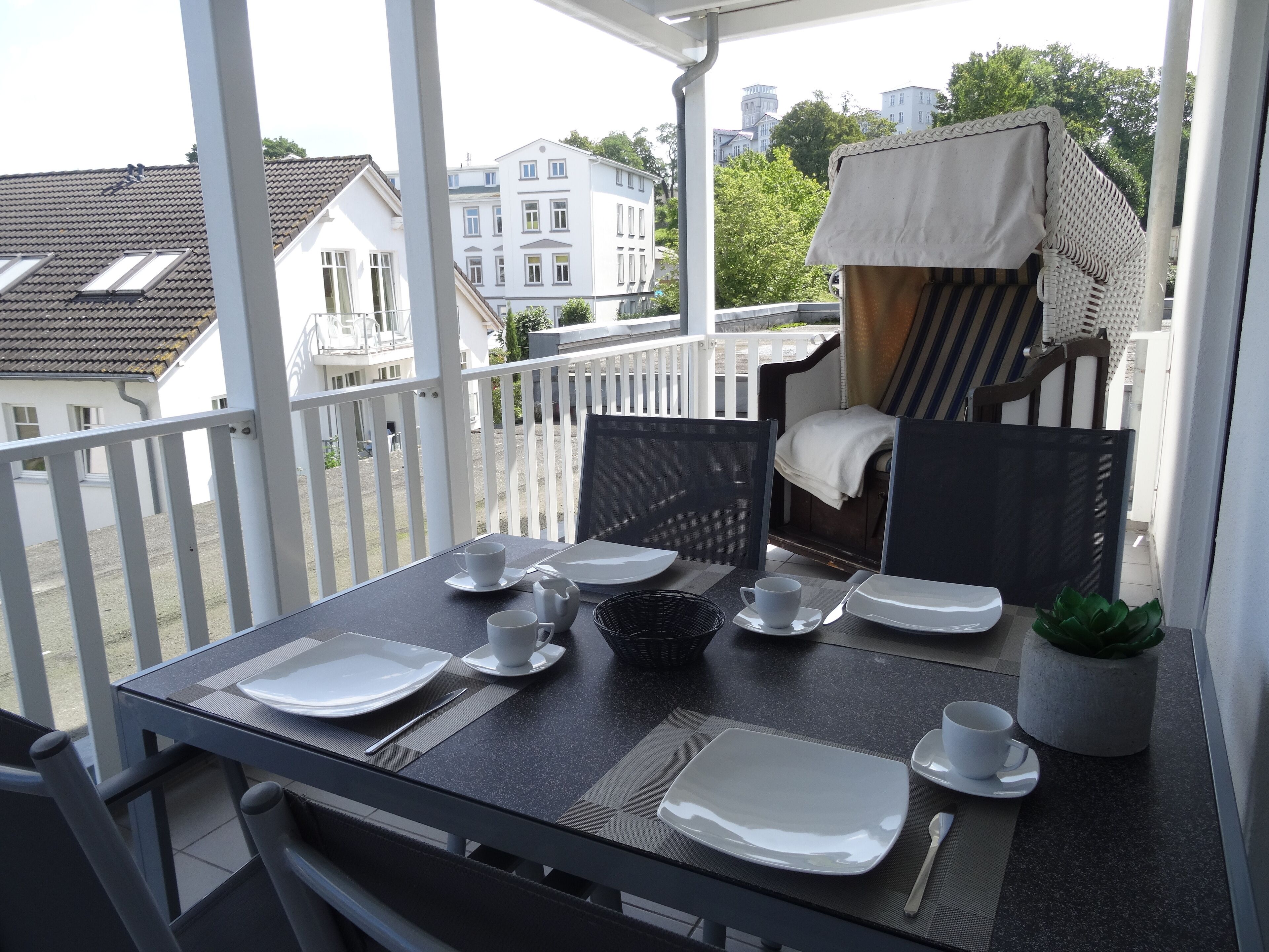Un balcon avec une table dressée pour deux personnes, une chaise et une petite plante en pot.