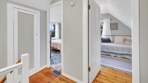 A narrow hallway leading to a bedroom with a sloped ceiling and a bed with patterned bedding.