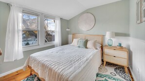 A bedroom with a bed, a bedside table, a lamp, and a window with curtains.