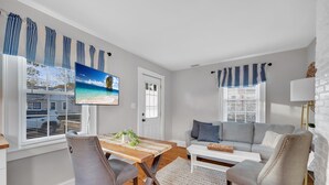 A living room with a wooden dining table, two grey upholstered chairs, a grey sofa, and a white coffee table.