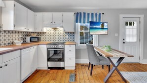 A kitchen with white cabinets, a microwave, an oven, and a dining table with a chair.