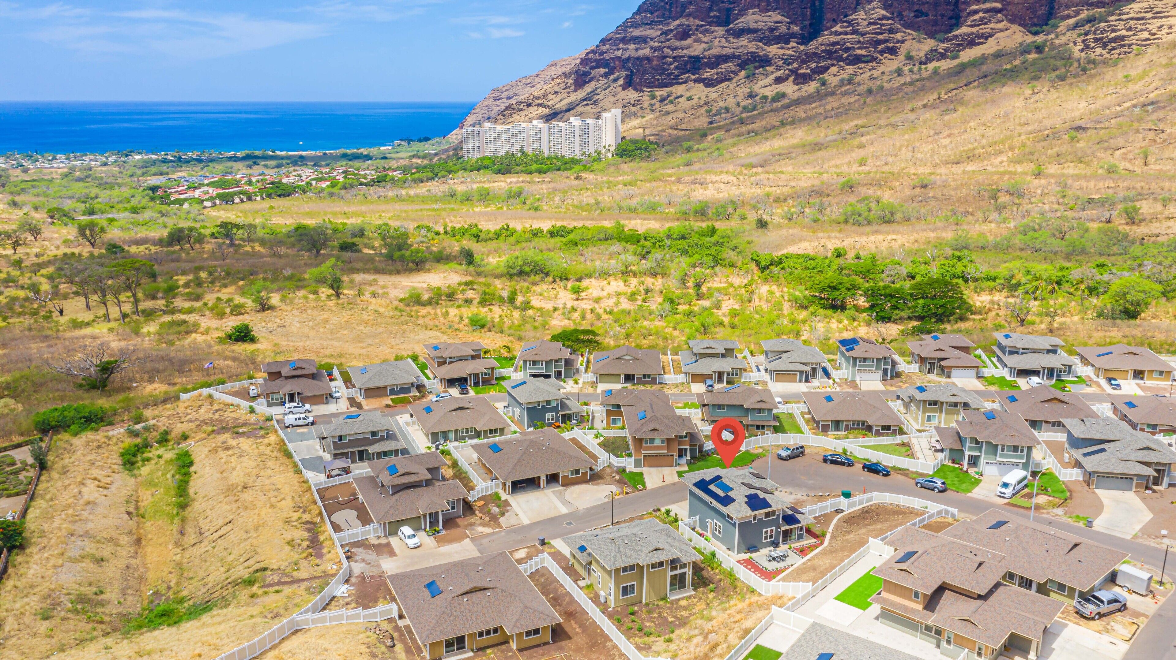 A residential area with houses, a road, and a view of the ocean and mountains in the distance.
