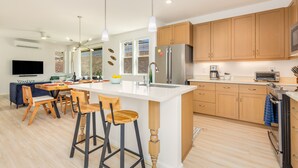Una cocina moderna con armarios de madera, una isla central, taburetes de bar y un comedor con televisor.
