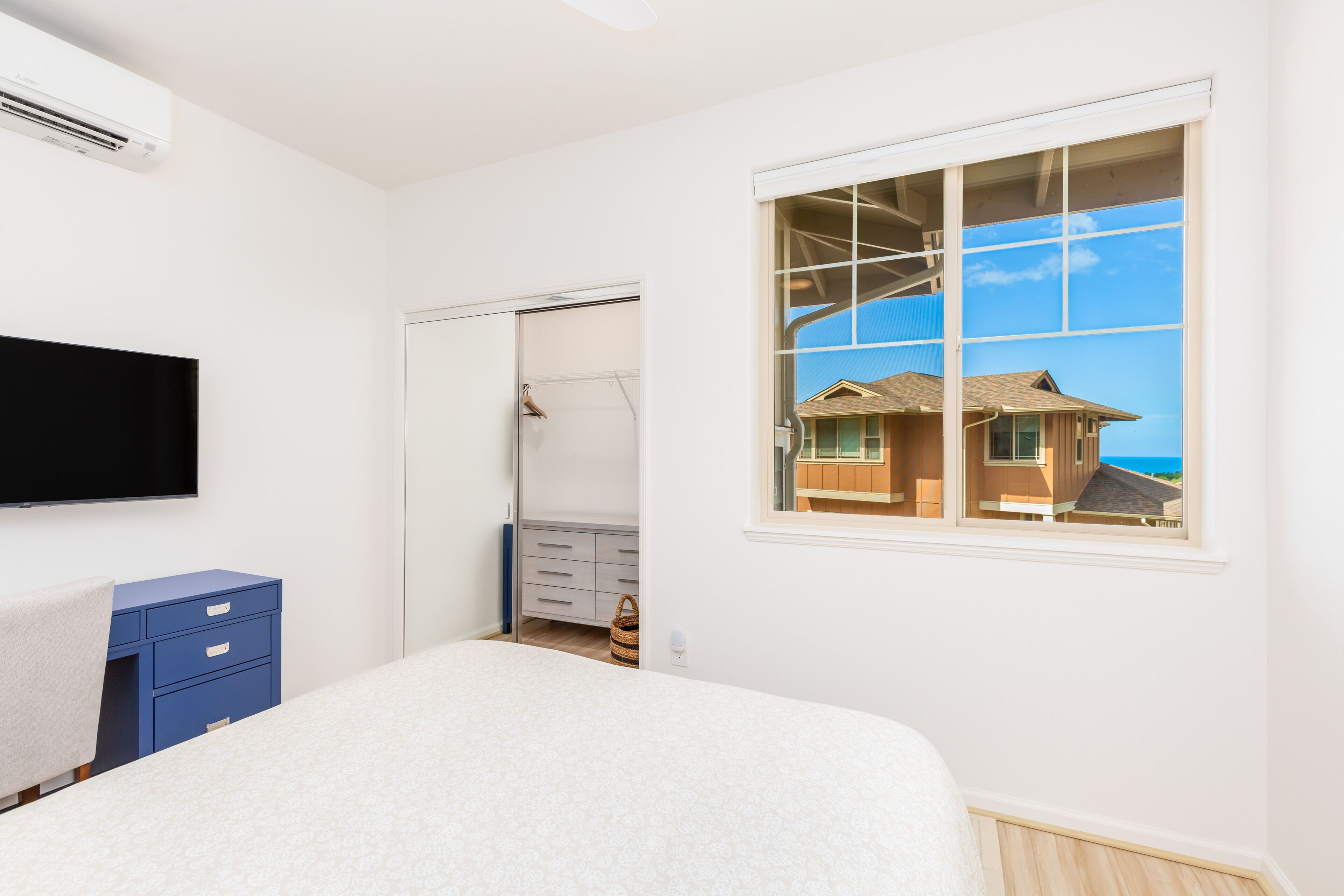 A bedroom with a bed, a wardrobe, a television, and a window with a view of a house.