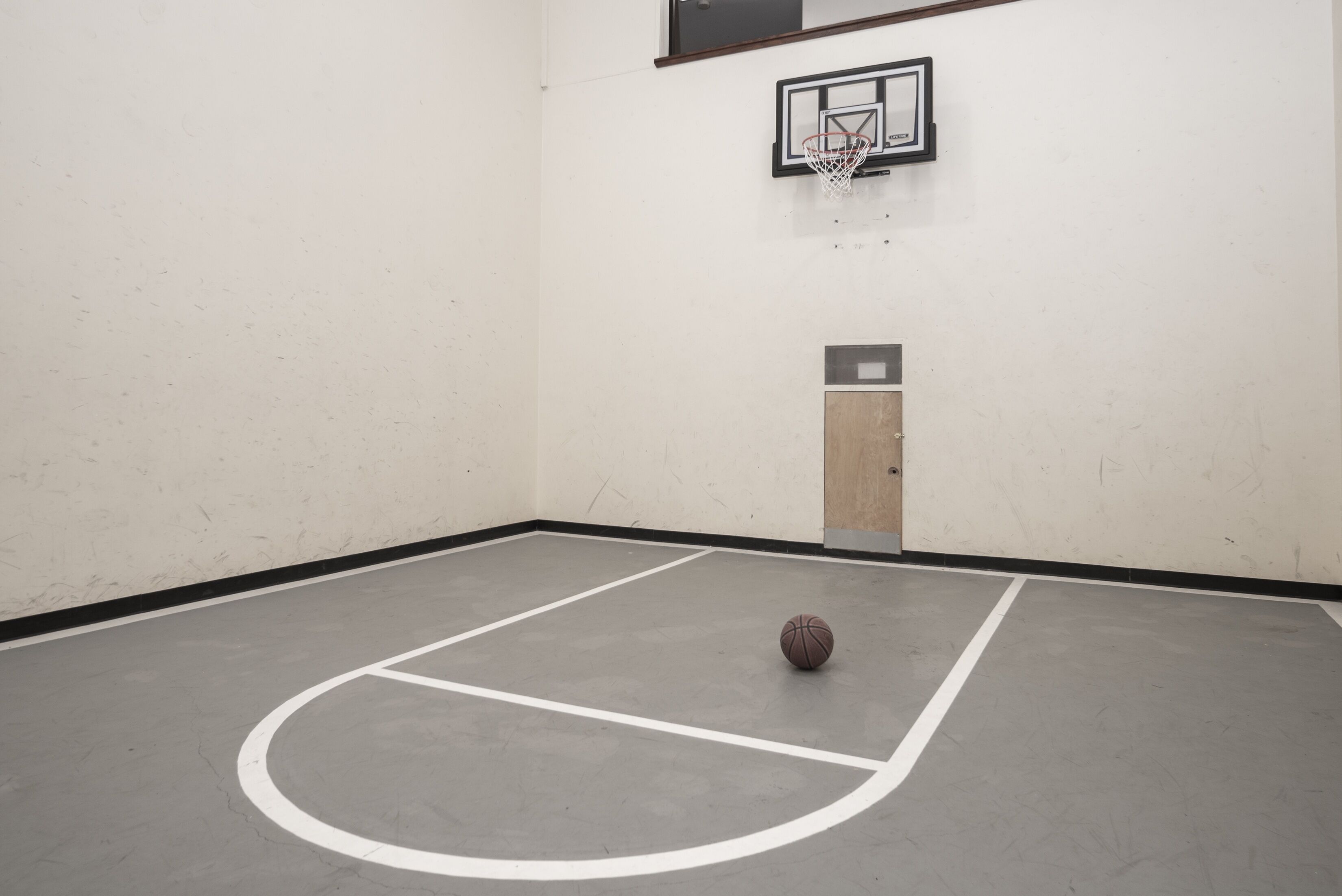 An indoor basketball court with a basketball hoop and a door.