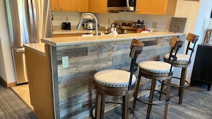 Una cocina con una isla de madera, dos taburetes de bar, electrodomésticos de acero inoxidable y armarios de madera.