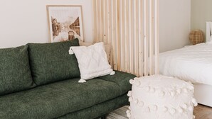 Une chambre moderne avec un canapé vert, un lit blanc, une cloison en lattes de bois et un tableau encadré au mur.