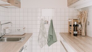 Une cuisine compacte avec des carreaux blancs, des armoires en bois, un évier en acier inoxydable et une serviette verte accrochée au mur.