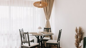 Un coin repas avec une table ronde, quatre chaises, un luminaire suspendu et des rideaux légers.