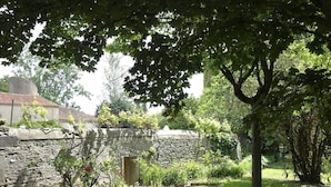 A stone wall with a small door, surrounded by greenery and trees.