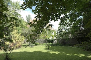 Un jardin bien entretenu, avec un mur de pierres, une pelouse verdoyante et un bâtiment partiellement recouvert de lierre.