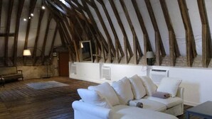 A loft-style room with a sloped ceiling, wooden beams, a white sofa, and a small table.