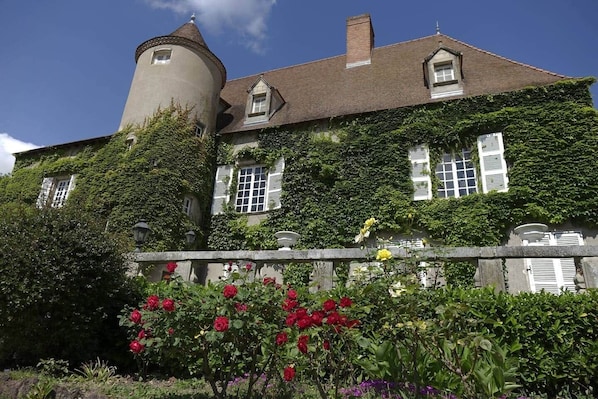 Un bâtiment historique doté d’une tour, de murs couverts de lierre et d’un jardin où poussent des rosiers.
