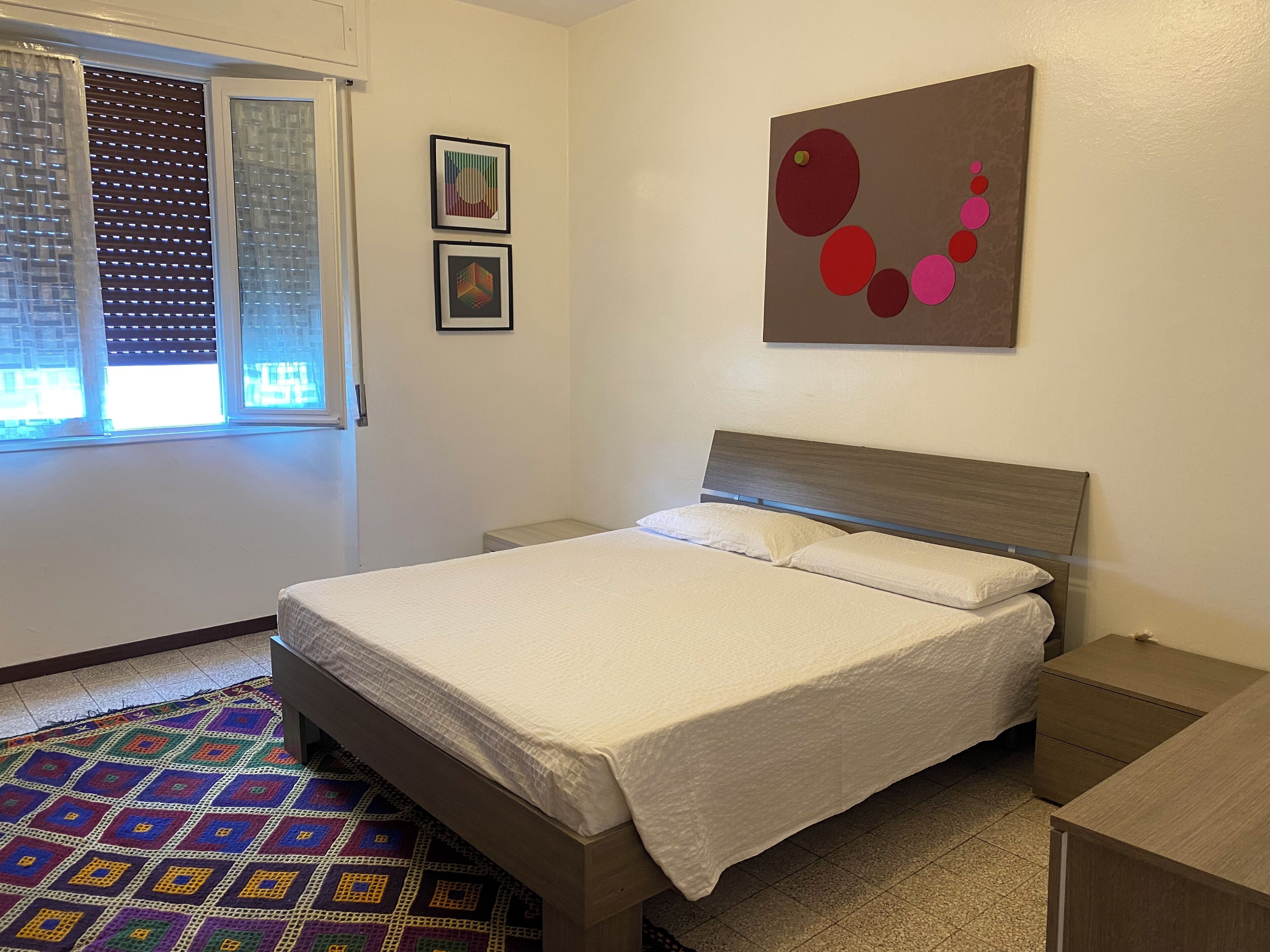 A neatly made bed with a wooden headboard, a bedside table, and a colorful patterned rug.