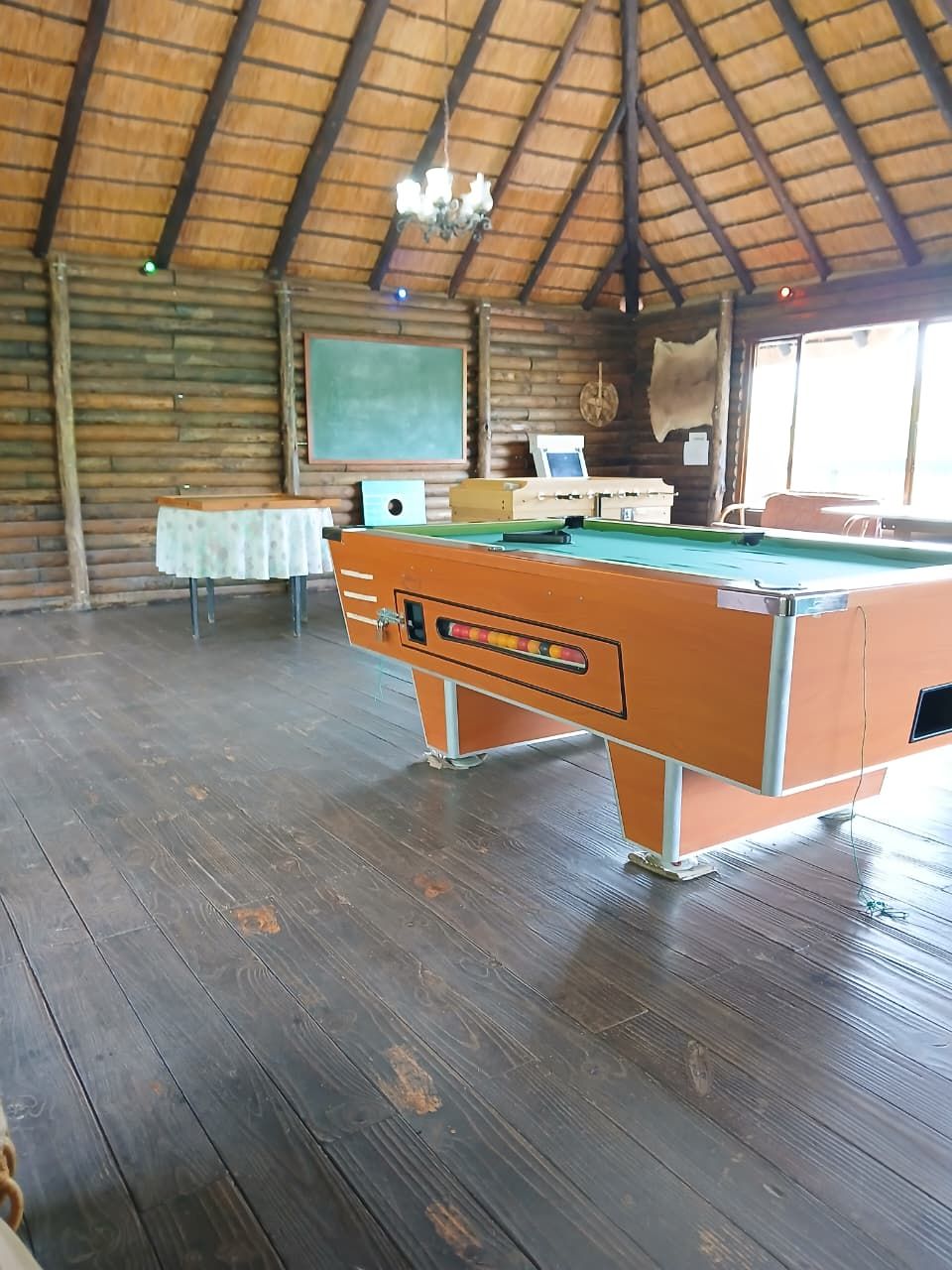 A pool table in a room with wooden floors and a thatched roof.