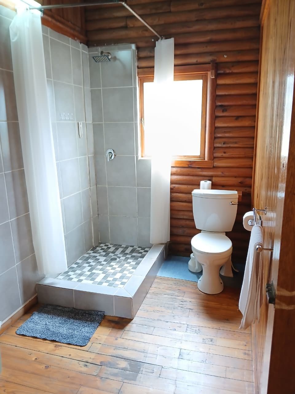 A bathroom with a shower, toilet, and a window.