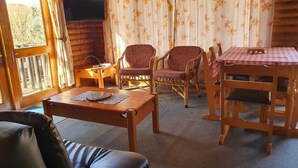 Ein gemütliches Blockhaus-Interieur mit einem Holztisch, zwei Korbstühlen, einer Couch und einem kleinen Tisch mit Unterlage.