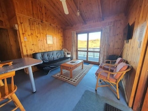 Ein Holzhäuschen im Inneren mit einer Couch, einem Esstisch und Stühlen, ein Balkon mit Aussicht.