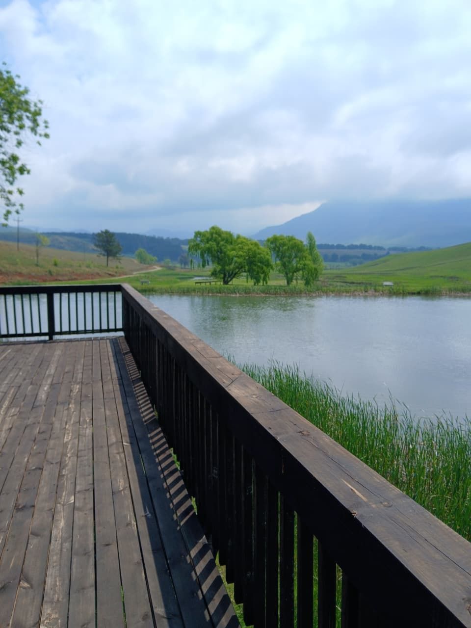 A wooden deck overlooking a calm lake with trees and hills in the distance.