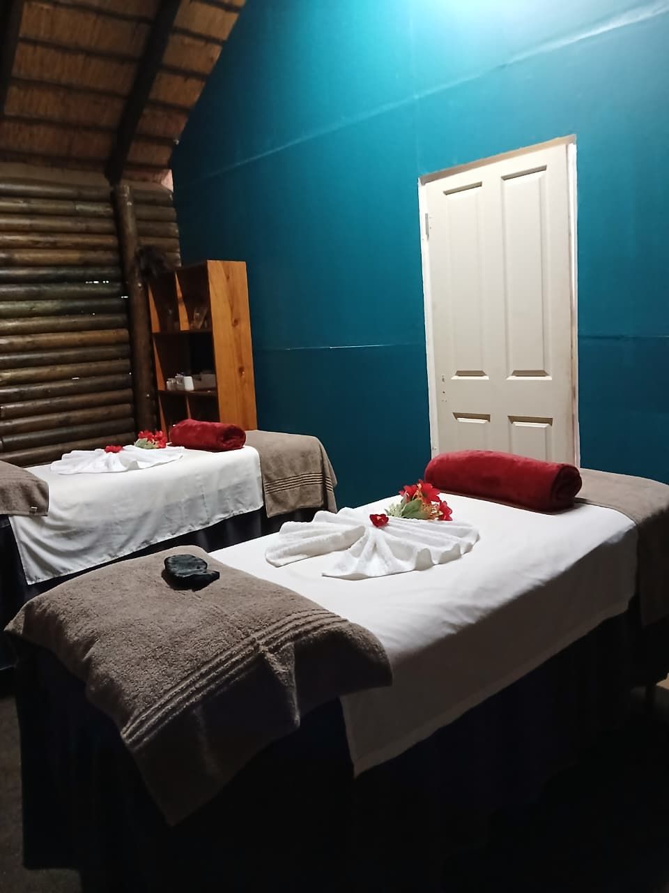 Two single beds with towels and flowers, a wooden door, and a blue wall.