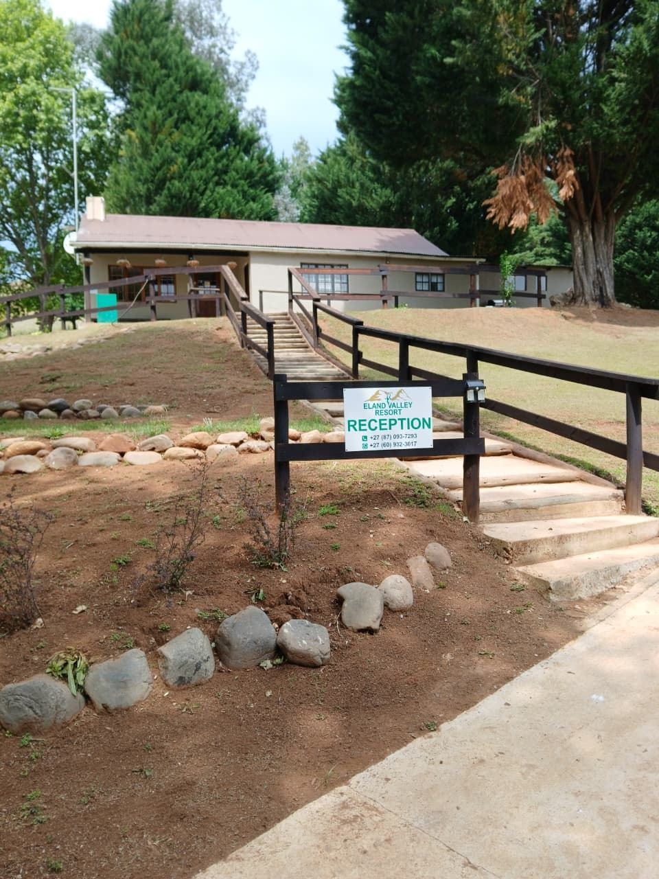 A reception area at Elan Valley Resort with a sign, a wooden fence, and a dirt path leading to a building.