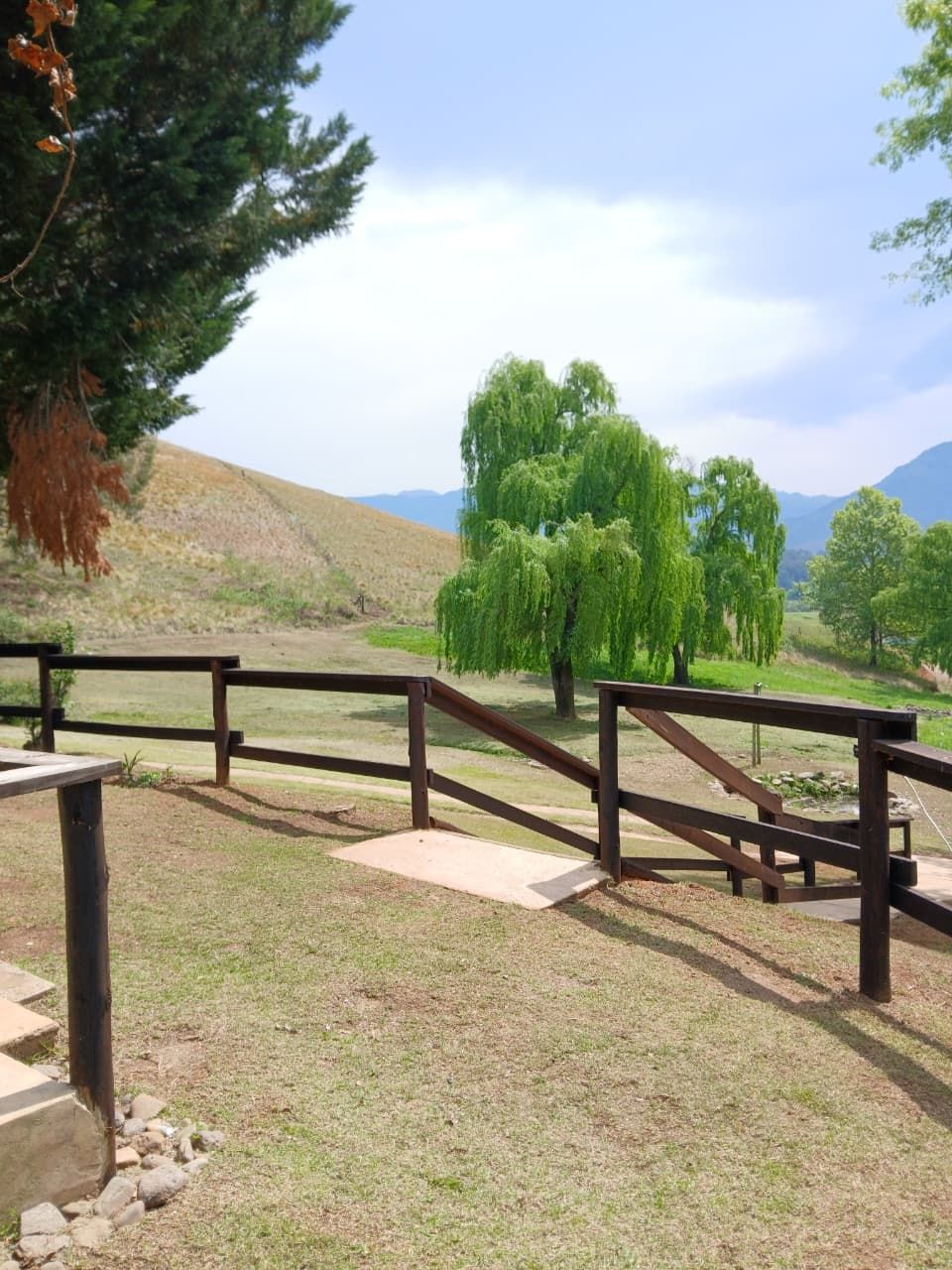 A park with a wooden fence, a picnic table, and a grassy area with trees.