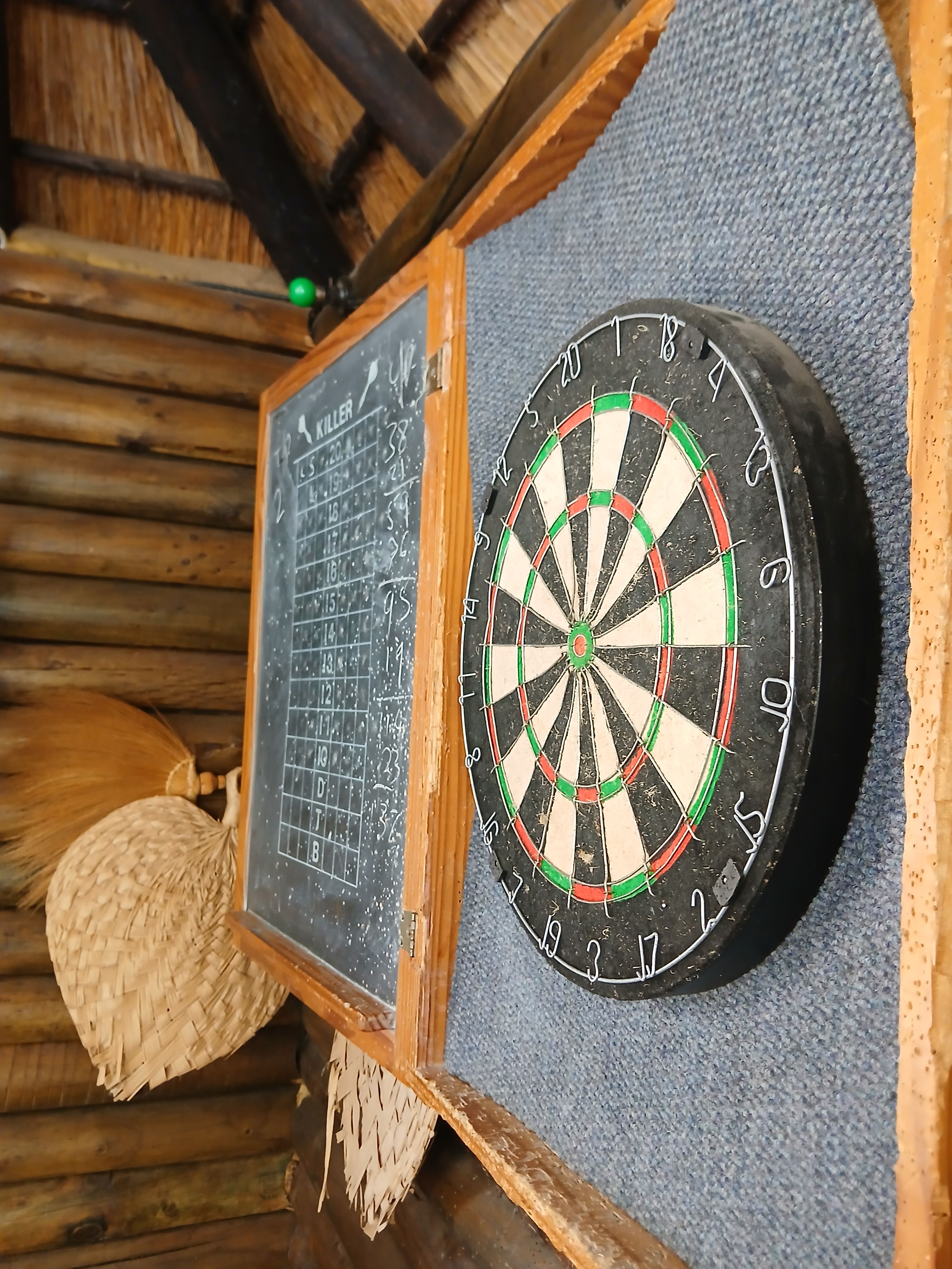A dartboard and a chalkboard with scores, both mounted on a wooden wall.