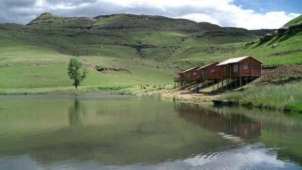 Eine Holzhütte mit einer Holzdar Terrasse und einem kleinen Steg, der in einen ruhigen See führt, umgeben von sanften Hügeln.