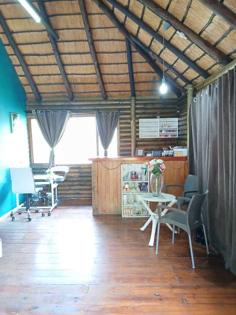 A wooden interior with a high ceiling, a dining area with chairs and a table, and a bar area with a shelf of bottles.