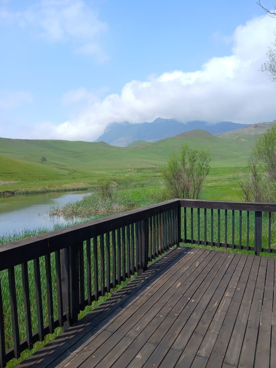 A wooden deck with a view of a lake and rolling hills.