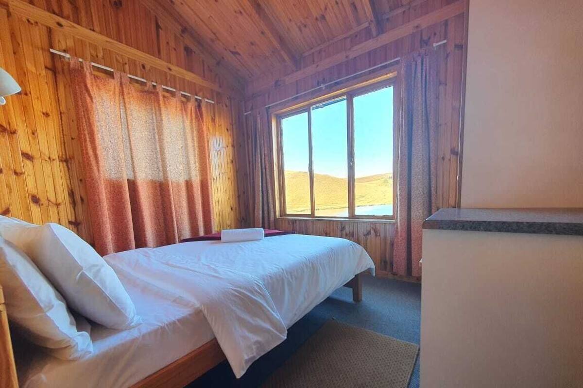 Una habitación de cabaña de madera con una cama, un ventanal con vista al desierto y un refrigerador.