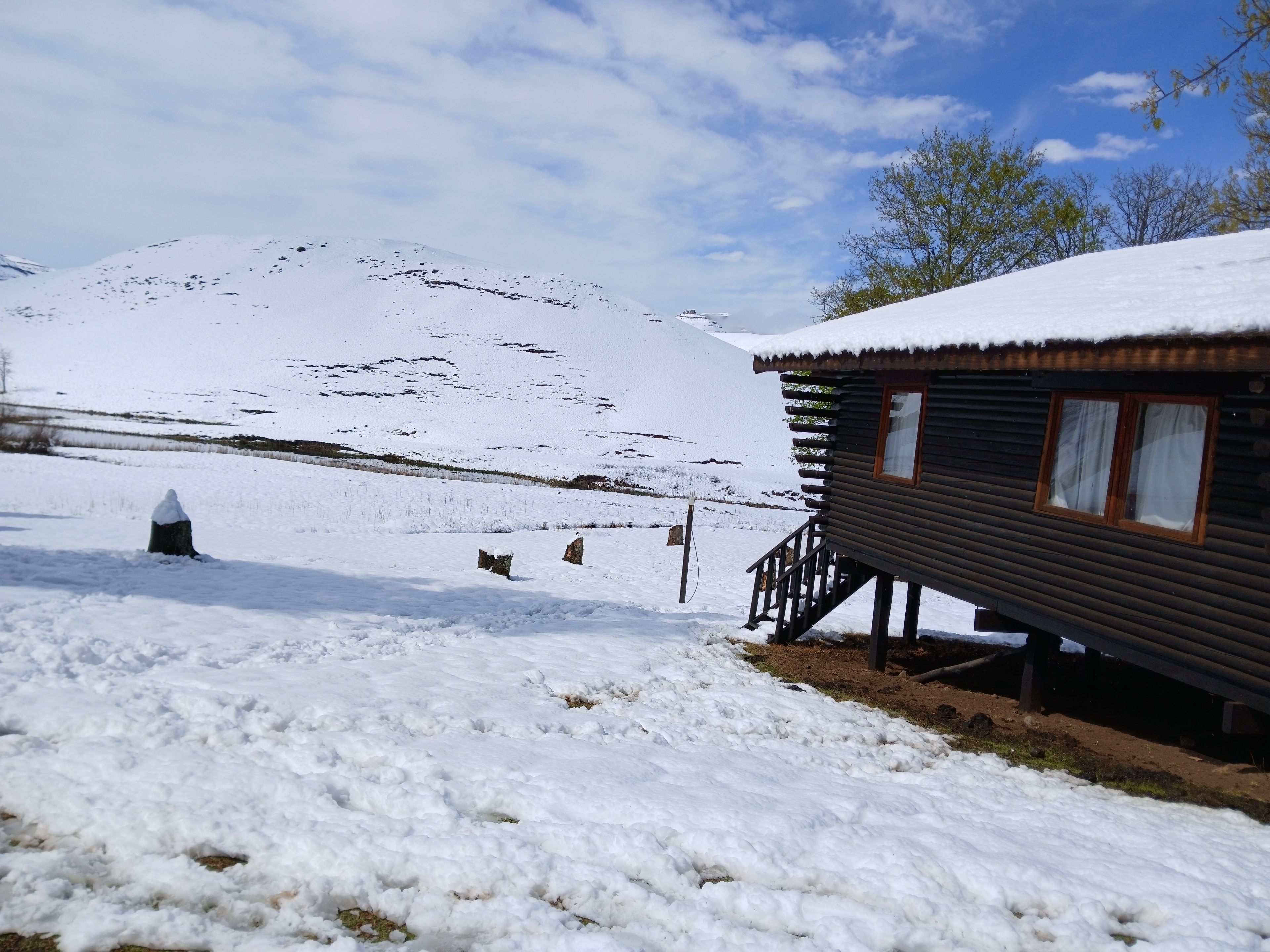 Eine Holzhütte mit einem schneebedeckten Dach, eingebettet in eine verschneite Winterlandschaft mit einem Berg im Hintergrund.