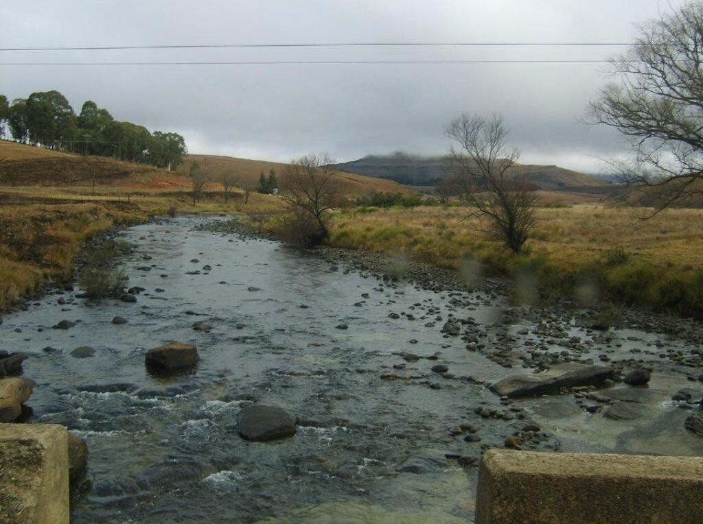 Une rivière traverse un paysage rural, avec des collines en arrière-plan.