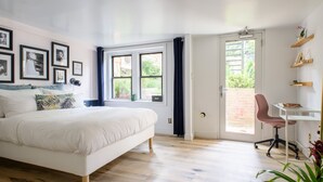 Un dormitorio con una cama, un escritorio y una silla. Hay ventanas y una puerta que da a un espacio exterior.