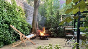 Una terraza de madera con un pozo de fuego, una silla de descanso y una mesa.