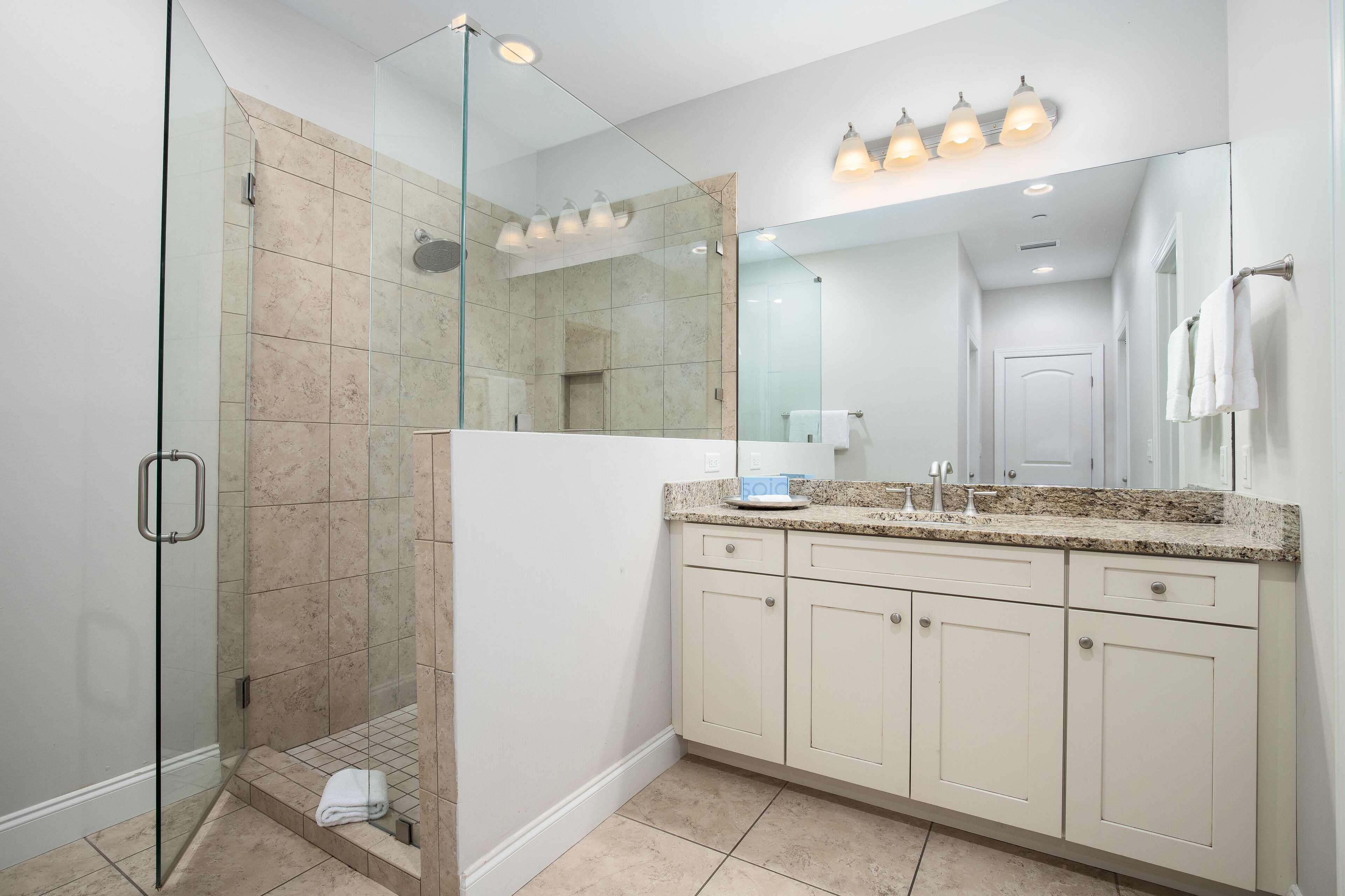 Une salle de bain moderne avec une douche à parois de verre, un grand miroir et un comptoir en granit.