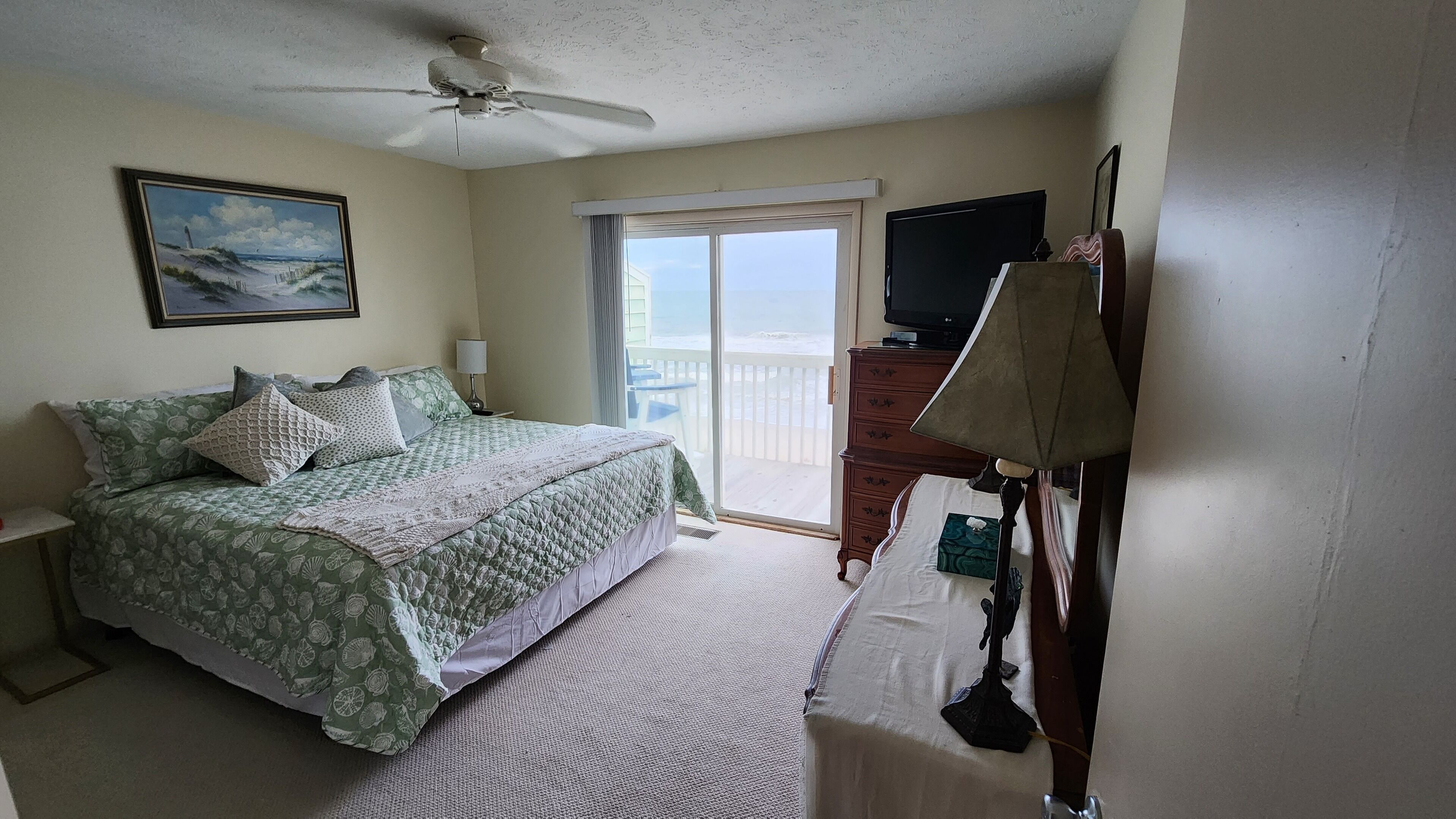 A bedroom with a bed, a dresser, a television, and a ceiling fan.