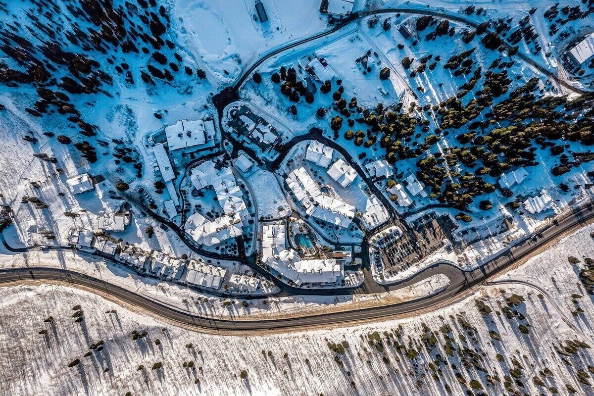 An aerial view of a snow-covered residential area with multiple buildings, roads, and a large body of water.