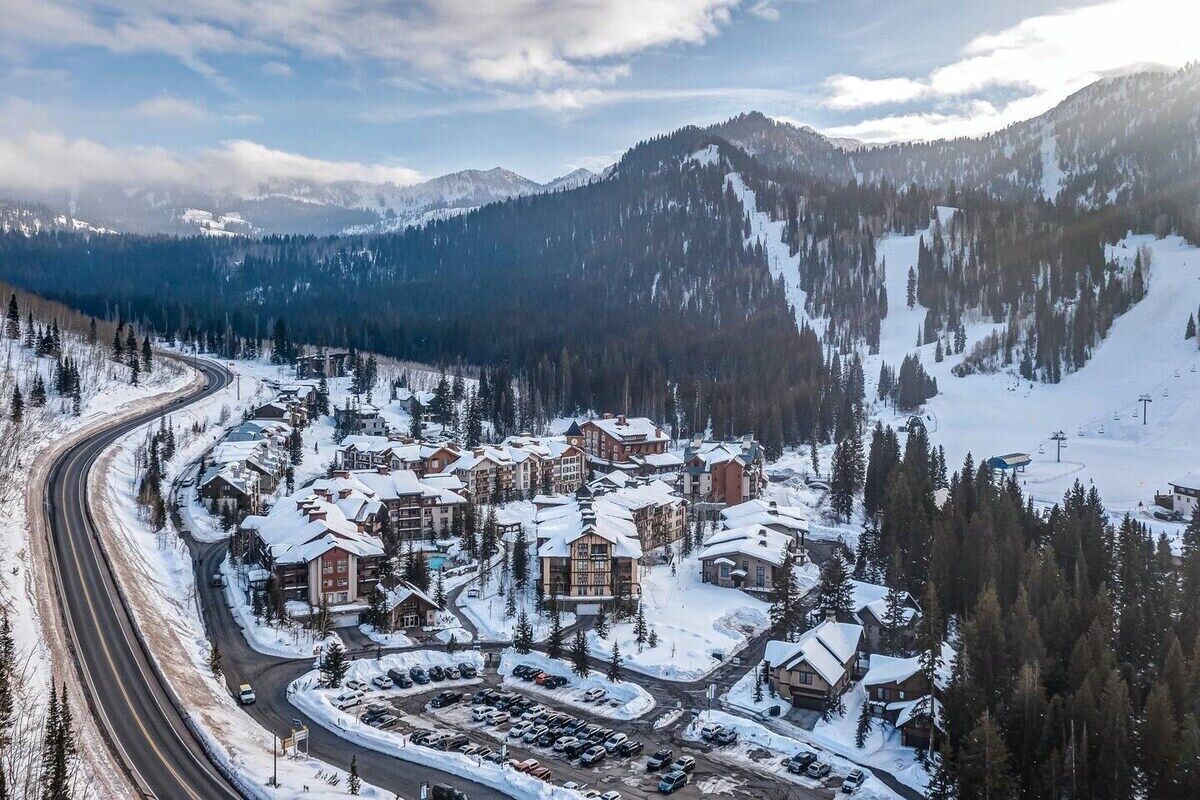 A snow-covered resort with multiple buildings, a parking area, and a winding road.