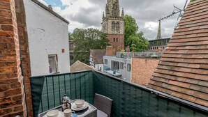 Ein Balkon mit Tisch für Zwei, mit Blick auf einen historischen Kirchturm und die umliegenden Gebäude.