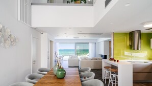 Eine moderne Küche mit grüner Rückwand, einem Holzespeisebereich mit Stühlen und Blick auf das Meer.