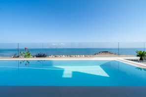 En klarblå pool med utsikt över havet och en sandstrand.