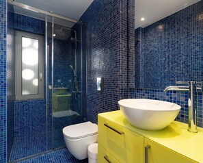 Ein Badezimmer mit blauen Mosaikfliesen, einer weißen Toilette, einem gelben Waschtisch mit einer weißen Spüle und einer Duschkabine aus Glas.