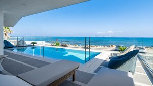 Ein moderner Infinity-Pool mit freiem Blick auf das Meer, eine Lounge mit einer Couch und einem Tisch sowie ein Glasgeländer mit Blick auf den Strand.