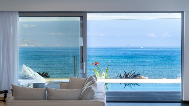 Ein modernes Wohnzimmer mit einem großen Glastür, das auf einen Balkon mit Meerblick führt.